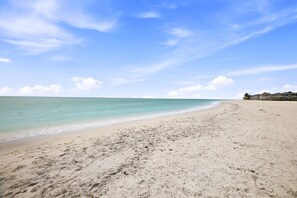 A beach with clear water, a sandy shore, and a building in the background. - Condo in canal-front community with private docks, heated pool, beach access (Englewood)