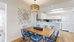 Een moderne keuken met witte kastjes, een houten eettafel en blauwe stoelen met kussens.