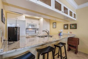 A kitchen with a marble countertop, stainless steel appliances, and a bar stool area. - Bayfront escape with beach access, and panoramic coastal views (Fort Myers)