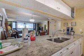 A kitchen with a granite countertop, stainless steel sink, and white cabinets. - Bayfront escape with beach access, and panoramic coastal views (Fort Myers)