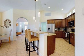 A kitchen with a central island, bar stools, wooden cabinets, and a microwave. - Newly designed home w/private heated pool, deck, AC heat recovery system (Naples)