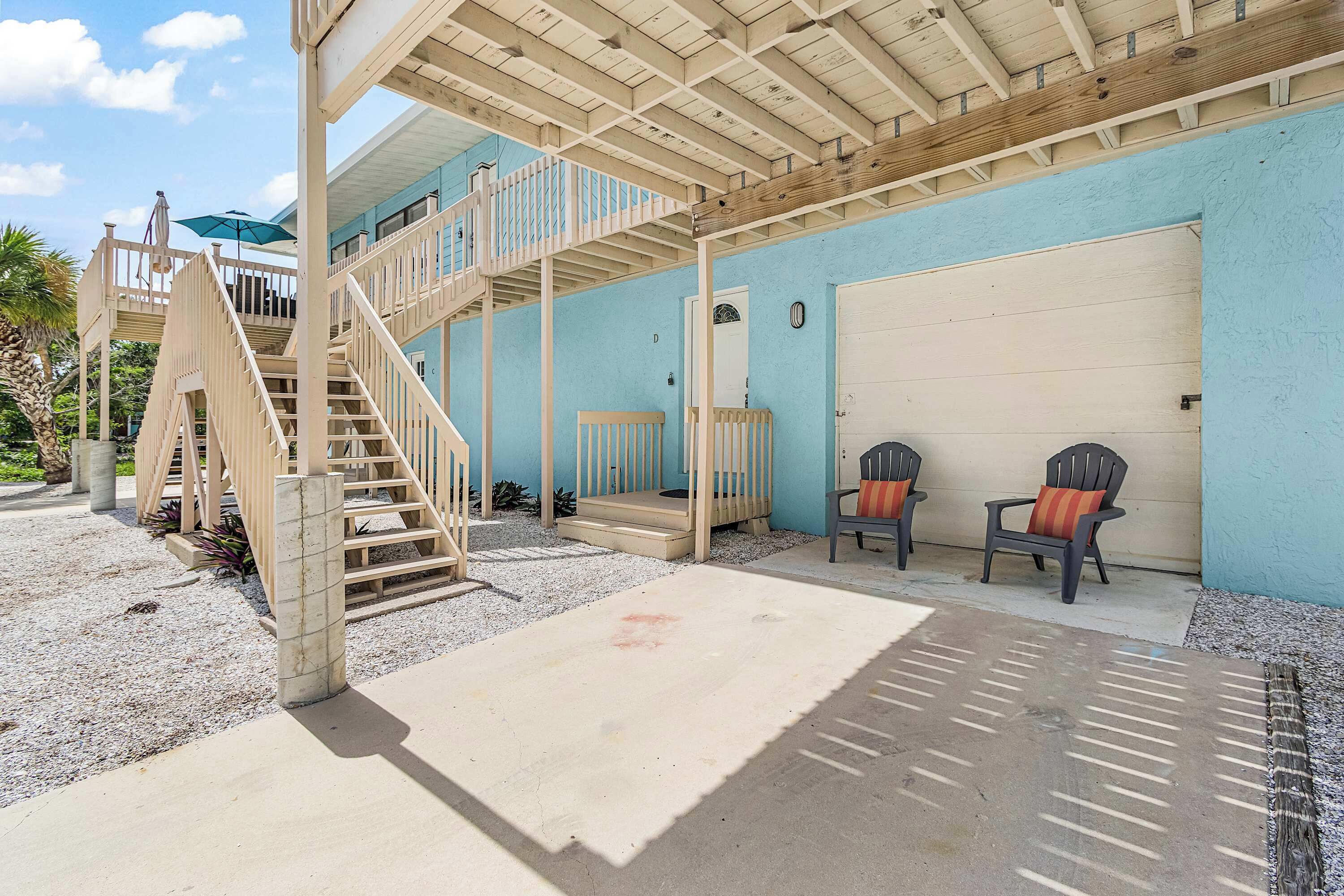 A two-story building with a covered patio area, a staircase, and a garage door.