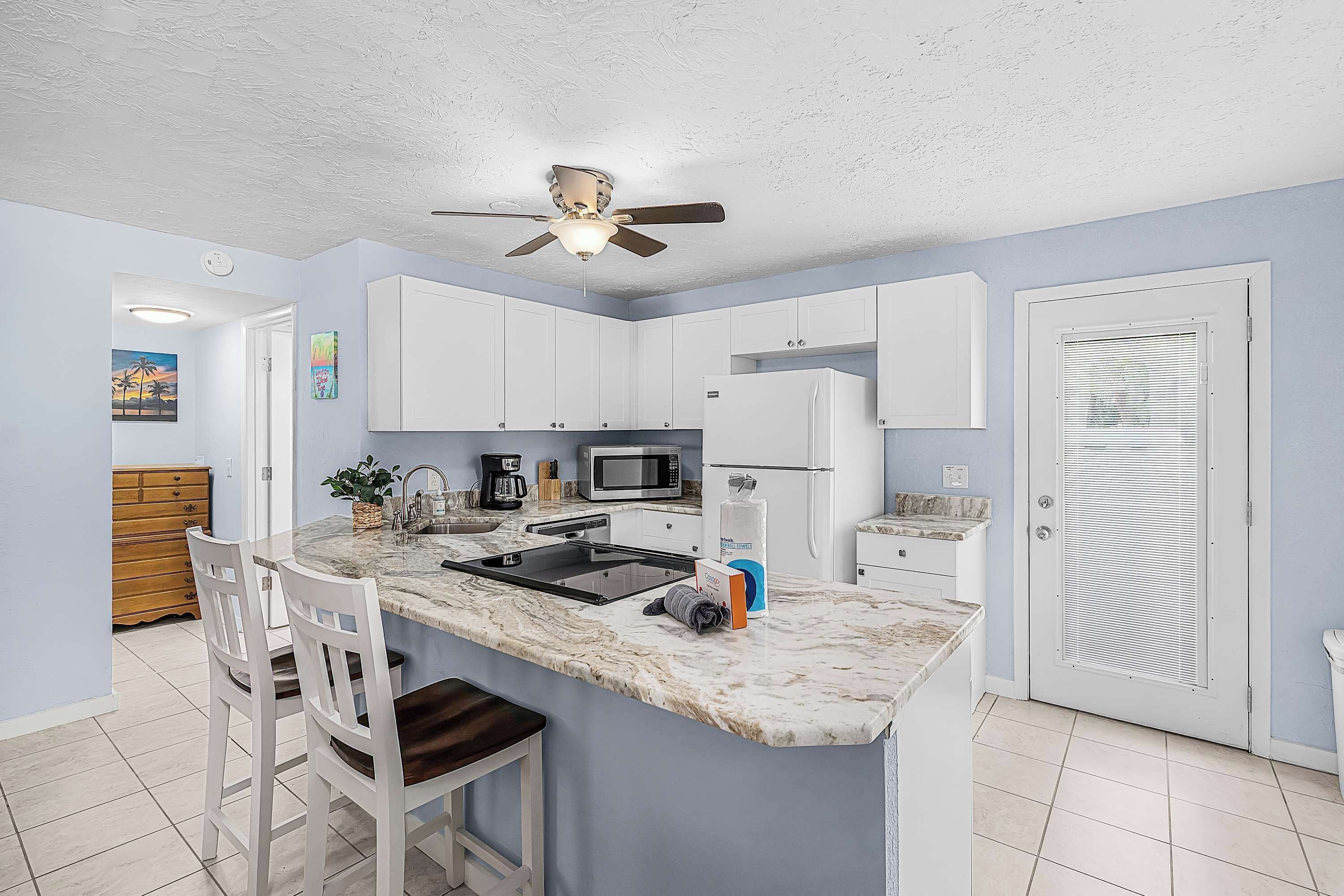 A kitchen with white cabinets, a marble countertop, a ceiling fan, and a door with blinds.