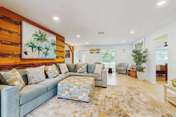 A living room with a sectional sofa, a coffee table, and a large painting on the wall. - Coastal home with private pool, arcade games, and firepit (Fort Myers)