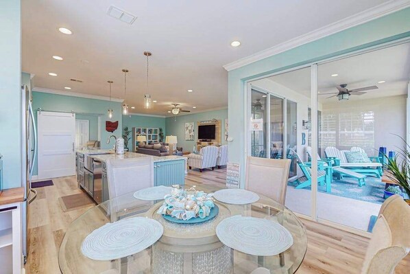 A modern kitchen with a central island, a dining area with a glass table, and a view of a pool through glass doors. - Chic Gulf Villa | Pools, Hot Tub, Sports Courts, Fishing Pier | Mins to Beach (Fort Myers)