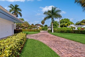 A paved pathway leading to a residential area with a white garage, well-maintained lawns, and palm trees. - Quiet and Breezy Bungalow near Beach w/ Screened Lanai & Gourmet Kitchen (Naples)