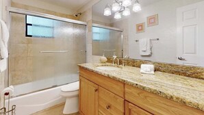 Un bagno con doccia vetrata, un water bianco, un lavabo su piano in granito, mobili in legno e un grande specchio illuminato.
