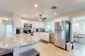 A modern kitchen with a granite countertop, stainless steel appliances, and a ceiling fan. - Quiet and Breezy Bungalow near Beach w/ Screened Lanai & Gourmet Kitchen (Naples)