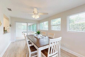 A dining area with a wooden table, white chairs, a ceiling fan, and large windows. - Quiet and Breezy Bungalow near Beach w/ Screened Lanai & Gourmet Kitchen (Naples)