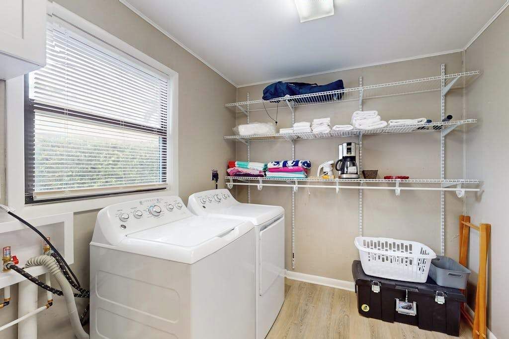 A laundry room with a washing machine, shelves with folded towels, and a laundry basket.