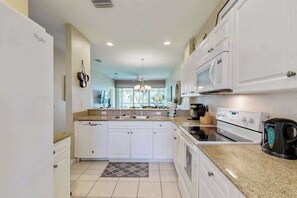 A modern kitchen with white cabinets, a built-in oven, a microwave, and a coffee maker. - Upgraded Greenlinks Golf Villas Condo | All-New Appliances | Luxe Pool & Spa (Naples)