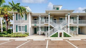 A multi-story building with balconies, a central staircase, and a parking lot. - Upgraded Greenlinks Golf Villas Condo | All-New Appliances | Luxe Pool & Spa (Naples)