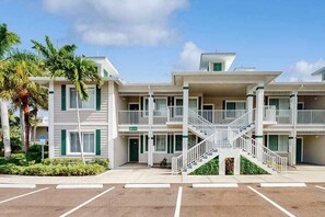 A multi-story building with balconies, a central staircase, and a parking lot. - Upgraded Greenlinks Golf Villas Condo | All-New Appliances | Luxe Pool & Spa (Naples)