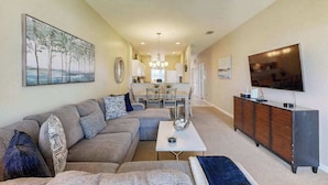 A living room with a sofa, coffee table, TV, and artwork on the walls. - Upgraded Greenlinks Golf Villas Condo | All-New Appliances | Luxe Pool & Spa (Naples)
