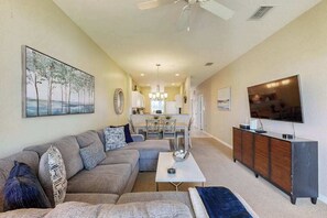 A living room with a sofa, coffee table, TV, and artwork on the walls. - Upgraded Greenlinks Golf Villas Condo | All-New Appliances | Luxe Pool & Spa (Naples)