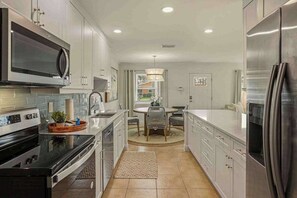 A modern kitchen with stainless steel appliances, white cabinetry, and a dining area with a round table and chairs. - Private heated-or-cooled pool, lush backyard, open-concept, upscale interiors (Naples)