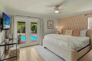 A bedroom with a bed, a ceiling fan, a TV, a pool view, and a framed picture on the wall. - Private heated-or-cooled pool, lush backyard, open-concept, upscale interiors (Naples)