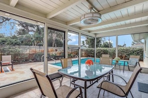 A covered patio with a glass table and chairs, a pool, and a view of the backyard.