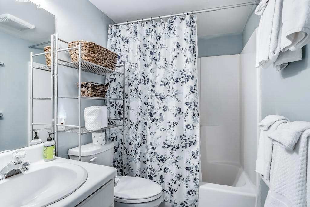 A bathroom with a shower curtain, a toilet, a sink, and shelves with baskets.