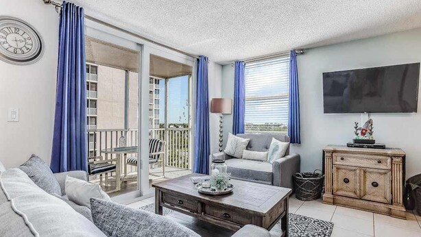 Un salon avec un canapé, une table basse, un téléviseur et un balcon agrémenté de rideaux bleus.