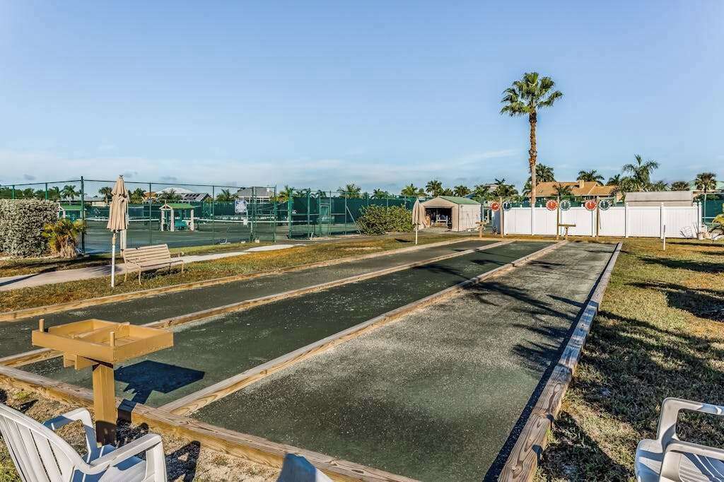 Ein Tennisplatz im Freien mit einer Holzbank, einer kleinen Schutzhütte und einer Palme.