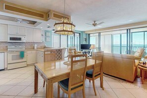 A modern kitchen with white cabinets, a dining table with chairs, a sofa, and a TV. - 10th-floor apt w/direct ocean views, private beach access, on-site pool, tennis (Bonita Springs)