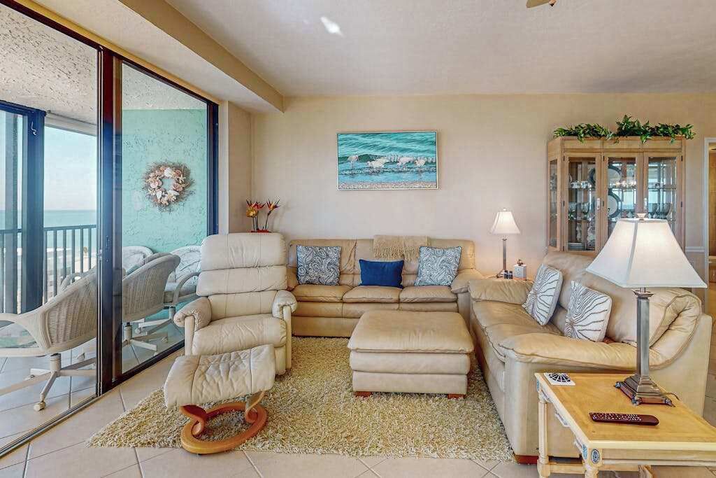 Un salon comprenant un canapé, des fauteuils, une table basse, une lampe et une vue sur l’extérieur, visible à travers une porte vitrée.