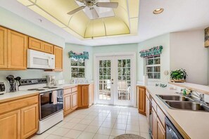A kitchen with wooden cabinets, a microwave, stove, and a ceiling fan. - Ground-floor condo on the golf course with decks, pools & AC - snowbird-friendly (Bonita Springs)