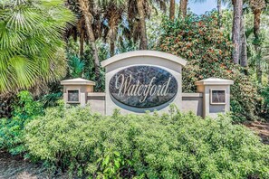 A sign with the name 'Waterford' surrounded by lush greenery and palm trees. - Ground-floor condo on the golf course with decks, pools & AC - snowbird-friendly (Bonita Springs)