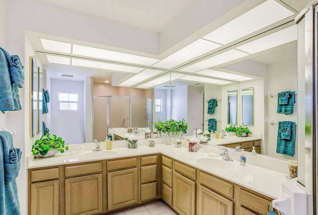 A modern bathroom with a large mirror, two sinks, wooden cabinets, and a shower area.