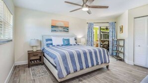 A bedroom with a bed, a nightstand, a ceiling fan, a window, and a door leading to another room. - Beautiful home with private pool & lanai - near beaches & parks (Bonita Springs)