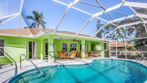 A swimming pool with a glass-enclosed patio area, a ceiling fan, and a view of palm trees. - Beautiful home with private pool & lanai - near beaches & parks (Bonita Springs)