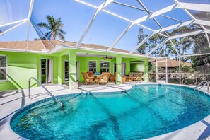 Une piscine avec un patio vitré, un ventilateur de plafond et une vue sur les palmiers.