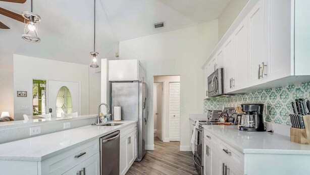 A modern kitchen with white cabinetry, a stainless steel refrigerator, a microwave, and a coffee maker. - Beautiful home with private pool & lanai - near beaches & parks (Bonita Springs)