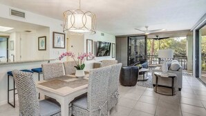 A modern dining area with wicker furniture, a central table, and a hanging light fixture. - 2nd-floor condo with private beach access, lanai, and access to heated pool (Bonita Springs)