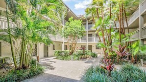 A courtyard with palm trees, a central walkway, and a multi-story building with balconies. - 2nd-floor condo with private beach access, lanai, and access to heated pool (Bonita Springs)