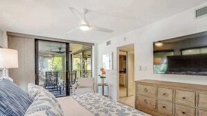 A bedroom with a bed, a TV, a ceiling fan, a dresser, and a sliding glass door leading to a balcony. - 2nd-floor condo with private beach access, lanai, and access to heated pool (Bonita Springs)