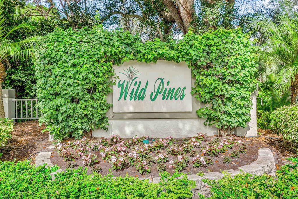 Un panneau sur lequel est inscrit « Wild Pines », entouré d’une végétation luxuriante et de plantes en fleurs.