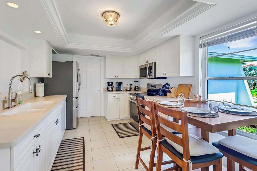 Een moderne keuken met witte kastjes, een zithoek met houten stoelen en een groot raam met uitzicht.