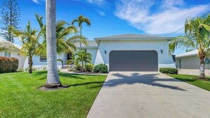 Une maison d’habitation avec un garage, une pelouse bien entretenue et des palmiers.