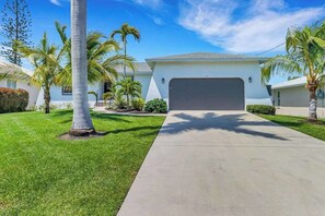 A residential house with a garage, a well-maintained lawn, and palm trees. - Serene & sunlit waterfront home with dock, patio, & incredible views - near golf (Bonita Springs)