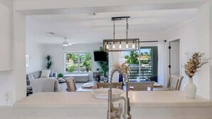 Une cuisine moderne dotée d’un îlot central, de luminaires suspendus et offrant une vue sur l’extérieur.
