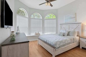 A bedroom with a bed, bedside tables, a ceiling fan, and large windows with blinds. - Modern Oasis with Pool, AC & WiFi, Minutes to Gulf Beaches! (Bonita Springs)