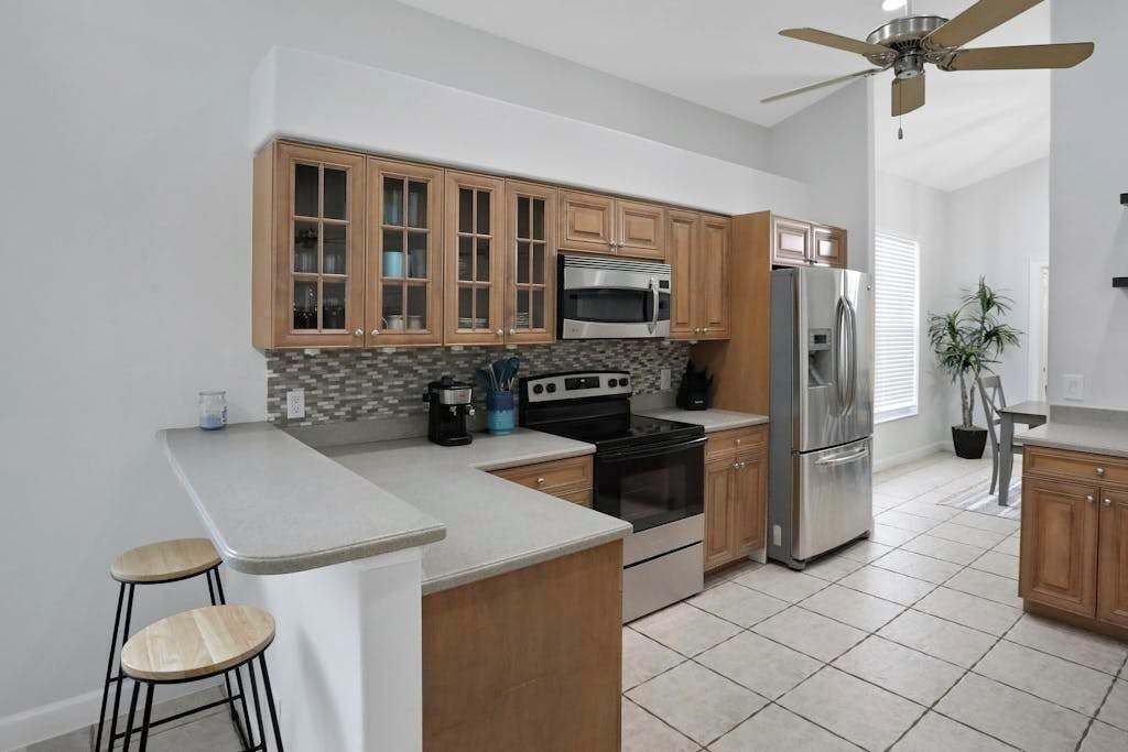 A kitchen with wooden cabinets, a microwave, a refrigerator, a stove, and a ceiling fan.
