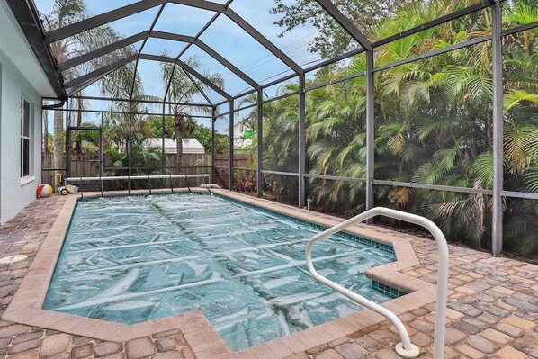 Une piscine entourée d’une paroi de verre, d’une terrasse en pierre et de plantes tropicales.