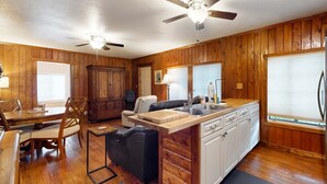 Une cuisine avec des meubles en bois, un coin repas avec une table et des chaises, un ventilateur de plafond et un réfrigérateur.
