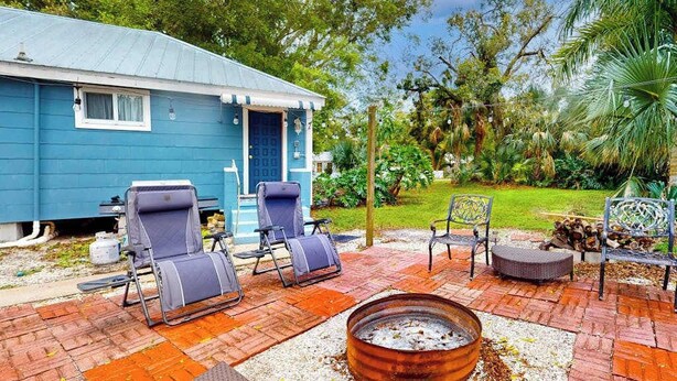 Une maison à l’extérieur bleu, avec une porte d’entrée et un patio aménagé avec du mobilier d’extérieur.