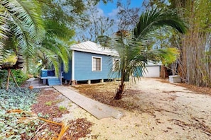 A small, single-story building with a blue exterior and a white roof, surrounded by dense tropical vegetation. - Classic dog-friendly cottage with kitchen, washer/dryer, & central AC (Bonita Springs)