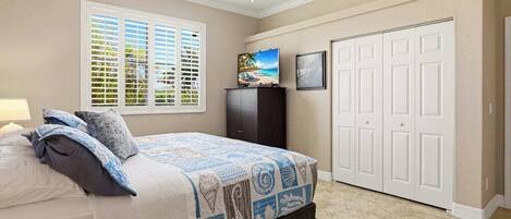 Un dormitorio con cama, ventilador de techo, televisor, armario y ventana con persianas.