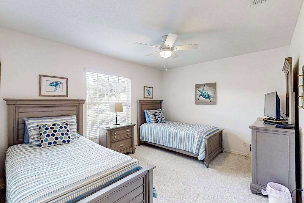 A bedroom with two beds, a ceiling fan, and artwork on the walls.